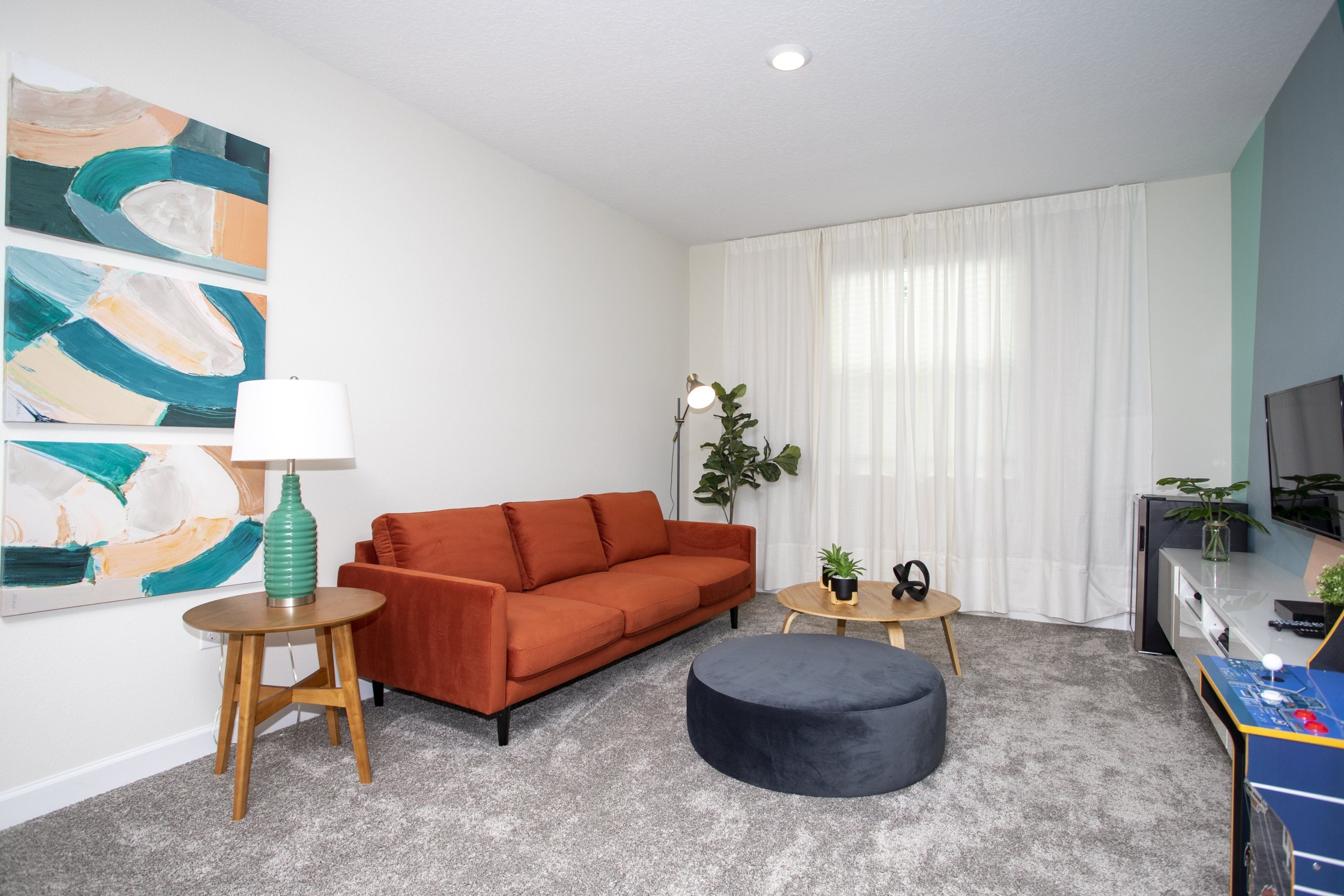 Een moderne woonkamer met een bank, poef, lamp en kunst aan de muur.