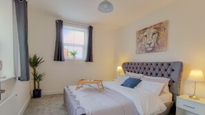 A bedroom with a bed, bedside tables, a window with curtains, a painting, and a potted plant. - Ye Olde Windmill Apartment Free Parking (York)