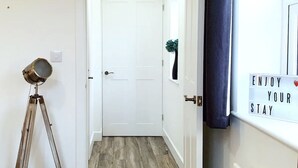 A hallway with a white door, a tripod with a light, and a sign that says "ENJOY YOUR STAY". - Ye Olde Windmill Apartment Free Parking (York)