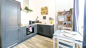 A modern kitchen with grey cabinets, a built-in oven, and a dining area with a white table and chairs. - Ye Olde Windmill Apartment Free Parking (York)