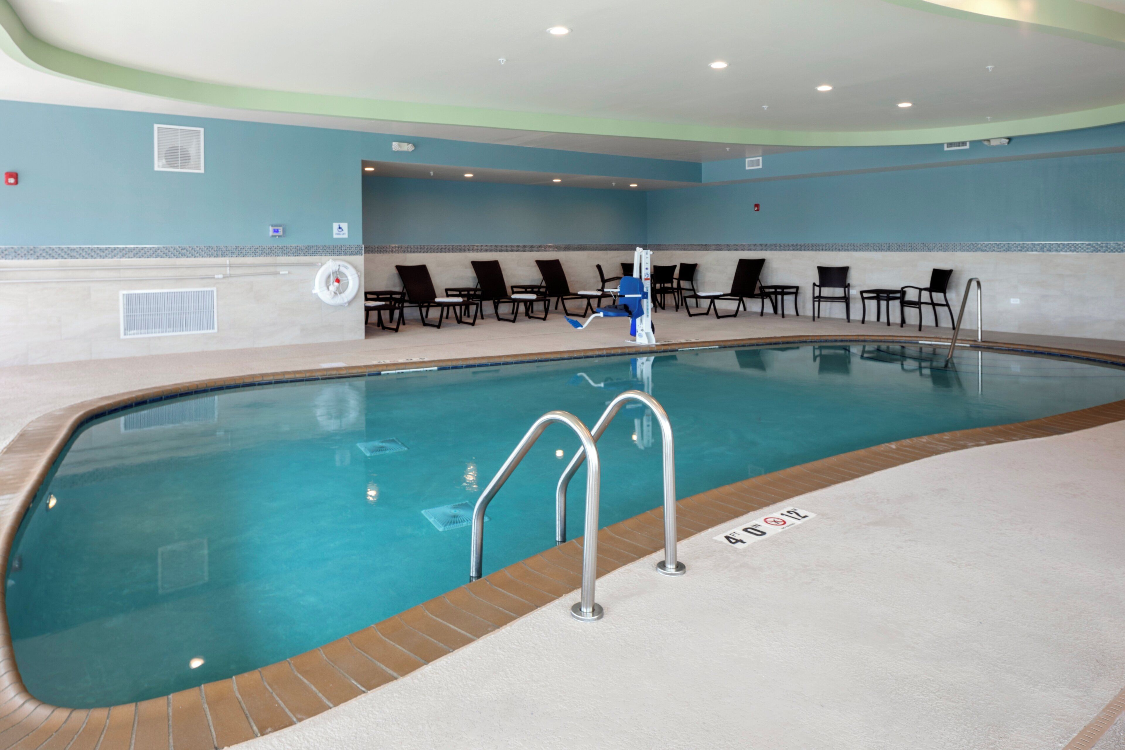 Una piscina interior con una silla de salvavidas, sillas de descanso y una escalera de piscina.
