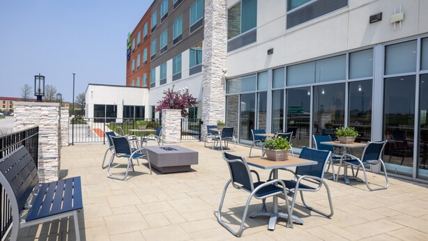 An outdoor patio area with seating arrangements, a stone wall, and a modern building with large windows. - Holiday Inn Express & Suites Bourbonnais East - Bradley by IHG (Bourbonnais)