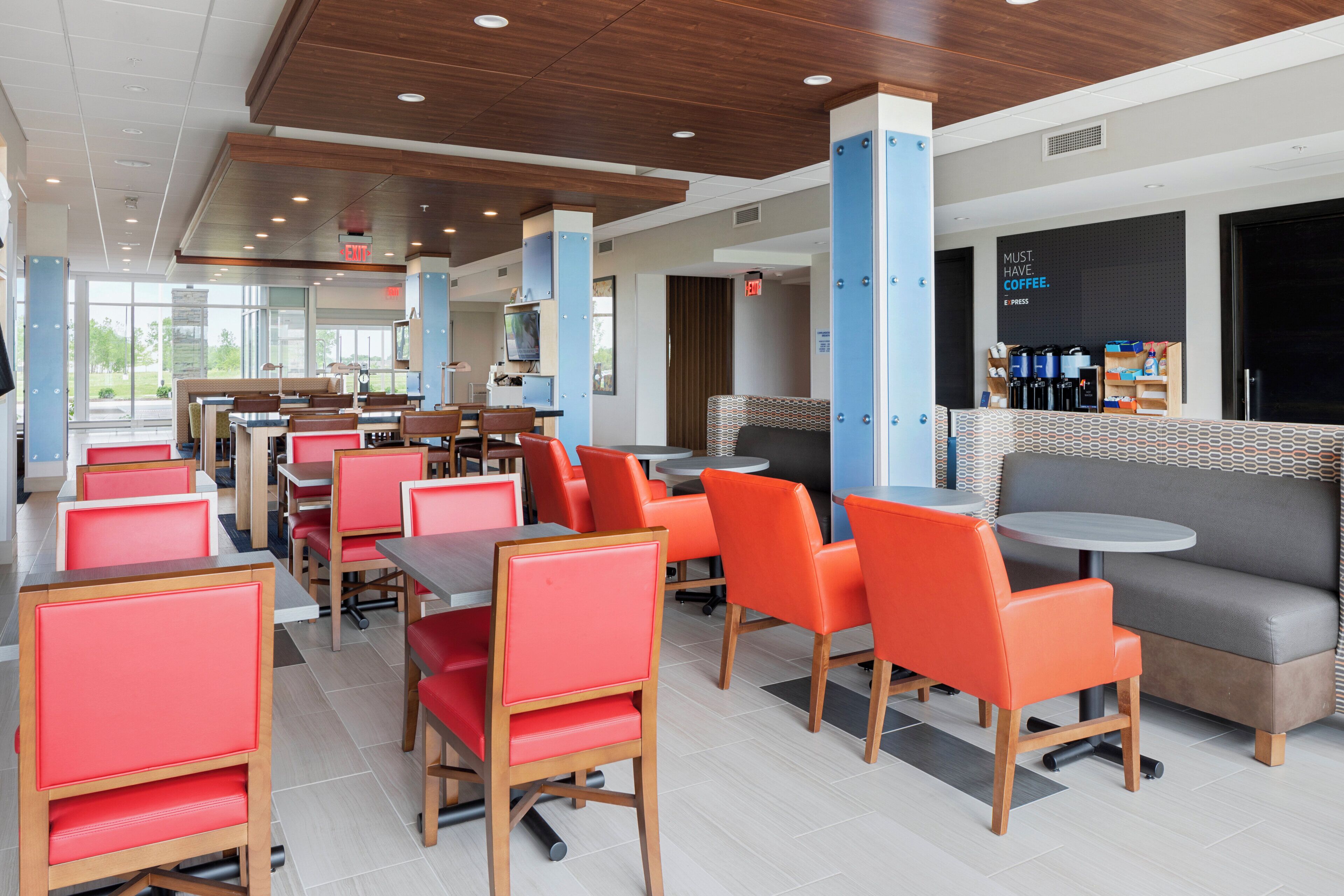 A modern cafeteria with red and grey seating, a coffee bar, and a large window offering a view of the outdoors.