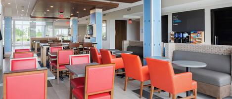 A modern cafeteria with red and grey seating, a coffee bar, and a large window offering a view of the outdoors.