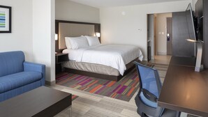 A hotel room with a bed, a blue sofa, a desk, and a TV. - Holiday Inn Express & Suites Bourbonnais East - Bradley by IHG (Bourbonnais)