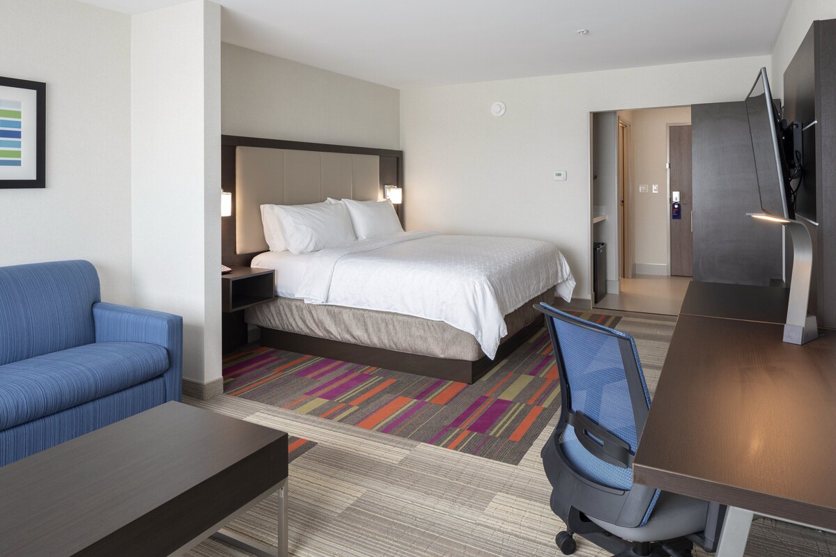 A hotel room with a bed, a blue sofa, a desk, and a TV.