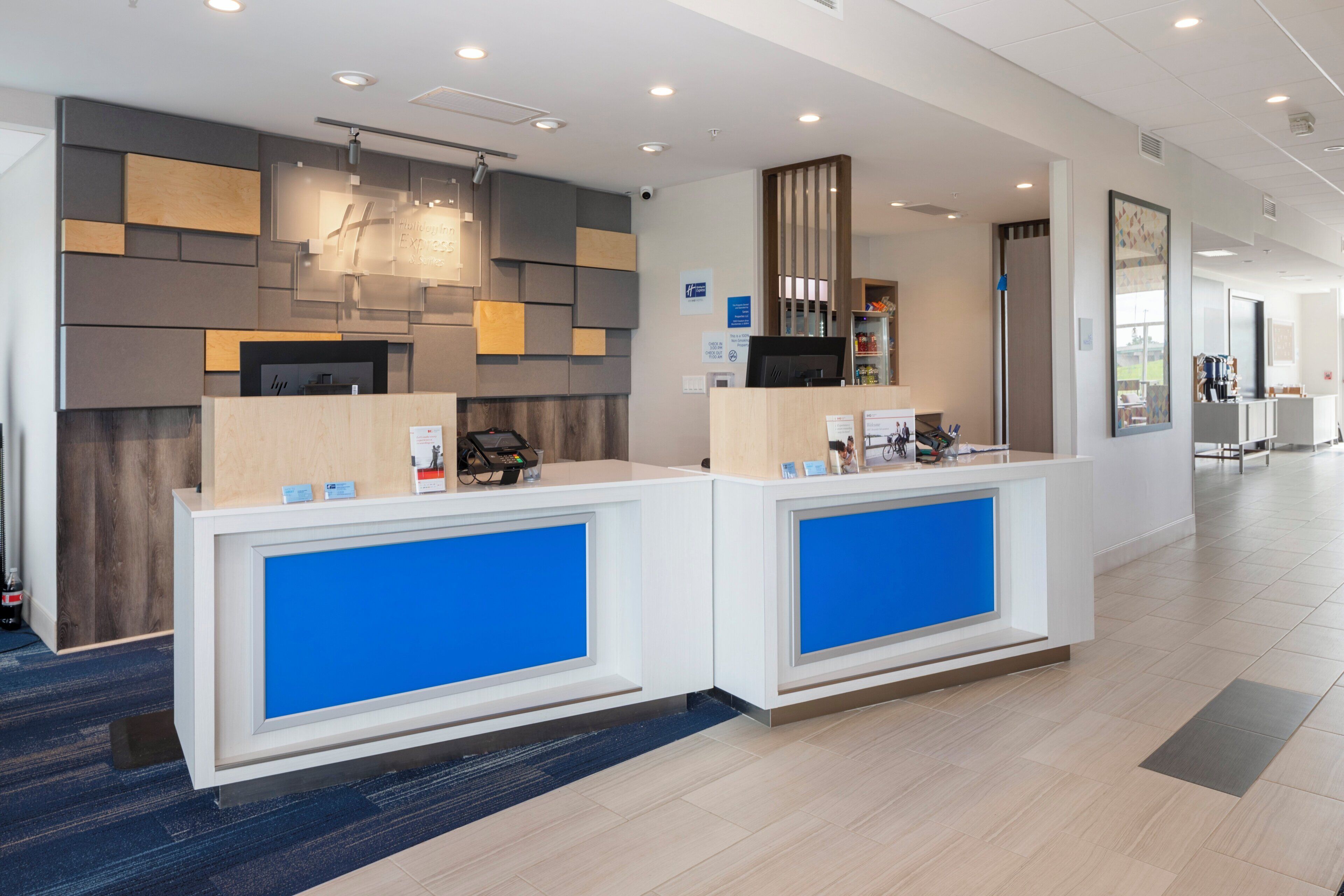 A reception area with two counters, a modern design with geometric wall panels, and a visible check-in kiosk.