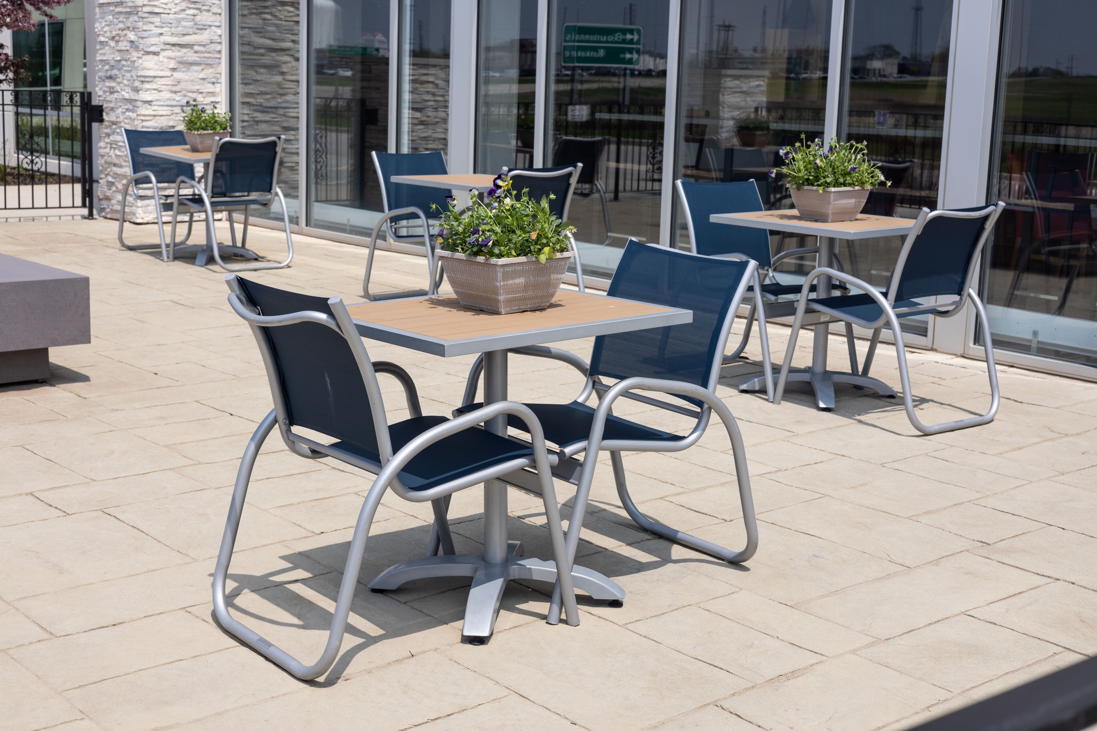 An outdoor patio area with metal-framed tables and chairs, some with potted plants.