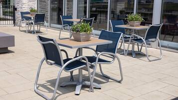 An outdoor patio area with metal-framed tables and chairs, some with potted plants.