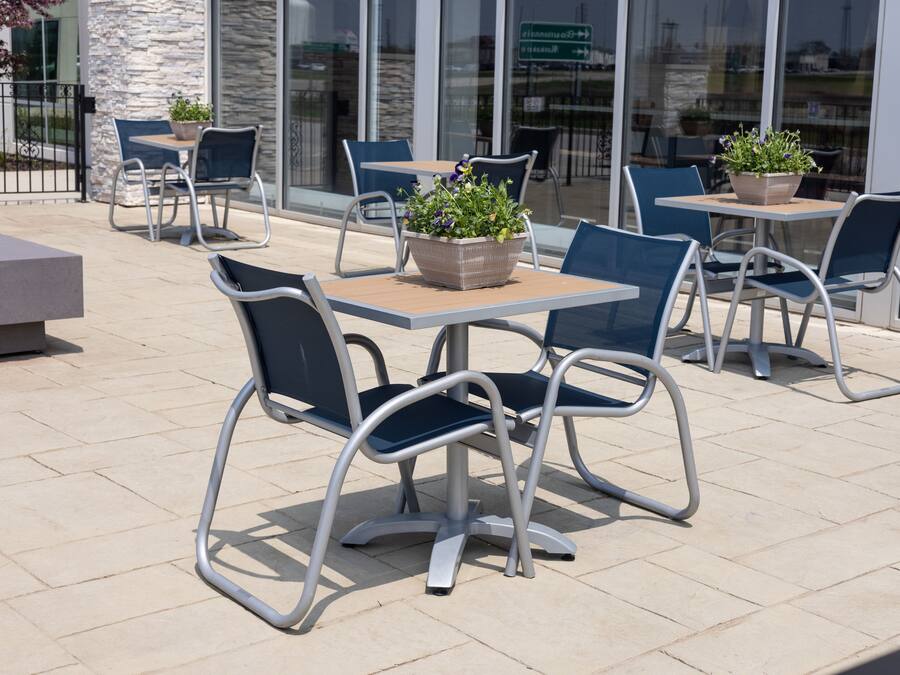 An outdoor patio area with metal-framed tables and chairs, some with potted plants.
