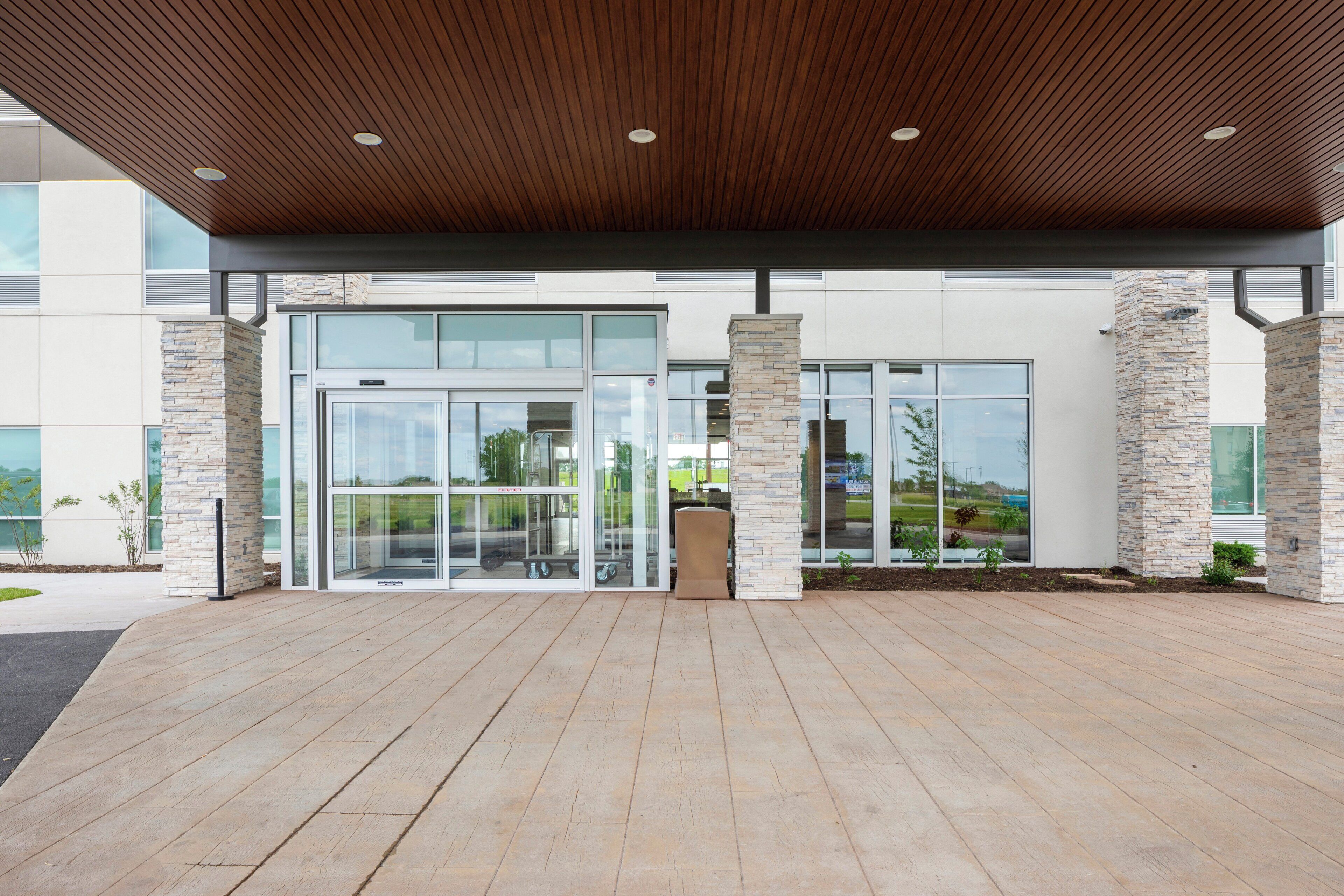 A modern building entrance with a wooden ceiling, glass doors, and stone pillars.