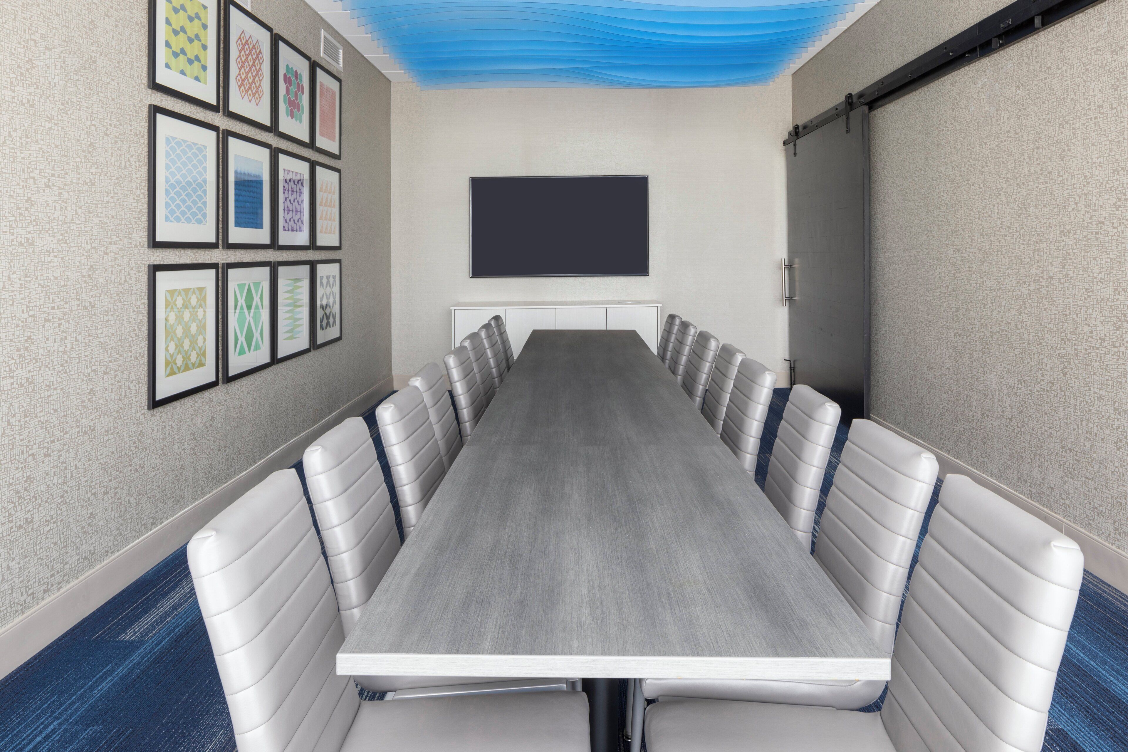 Ein Konferenzraum mit einem langen Tisch, gepolsterten Stühlen, einer Wandtafel und gerahmten Kunstwerken an den Wänden.
