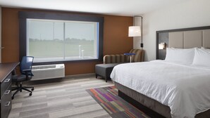 Ein Hotelzimmer mit einem großen Bett, einem Schreibtisch mit Stuhl, einem kleinen Tisch und einem Fenster mit Blick auf ein Feld.