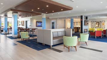 A hotel lobby with a seating area, a reception desk, and a dining area.