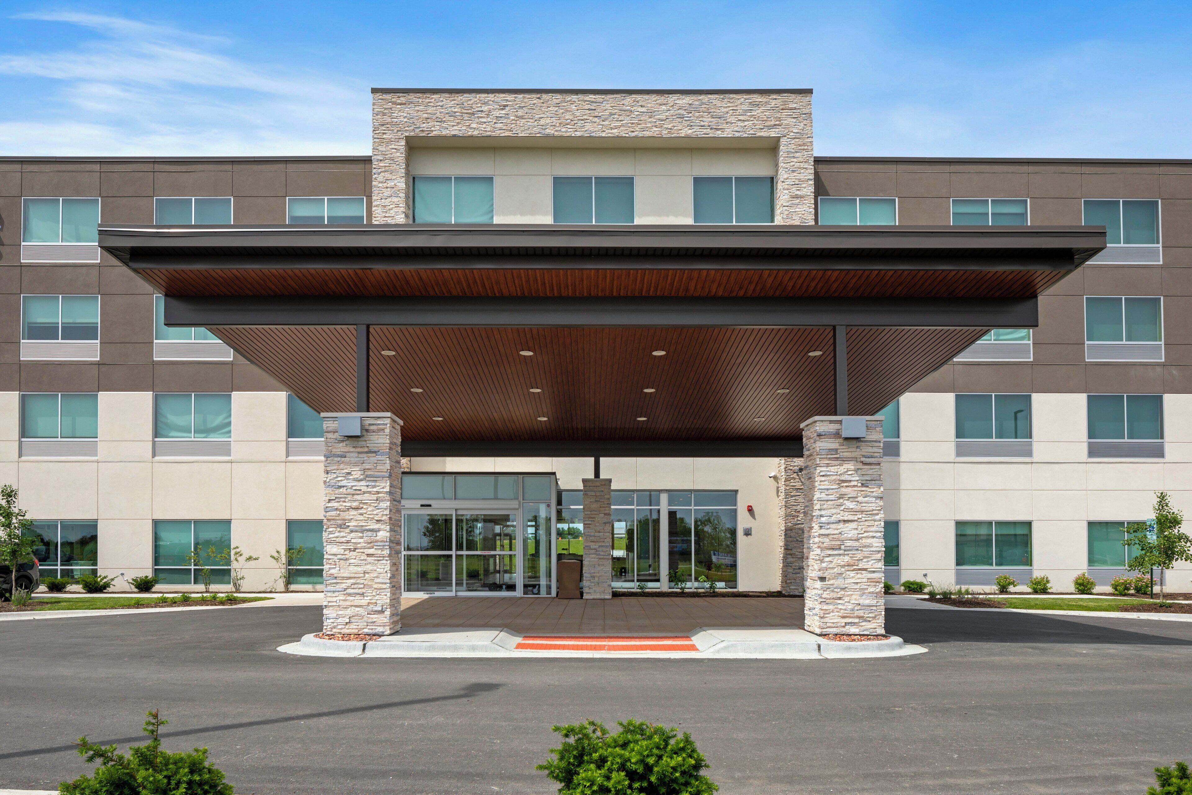 A modern building with a covered entrance, stone pillars, and a flat roof.