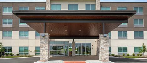 A modern building with a covered entrance, stone pillars, and a flat roof.