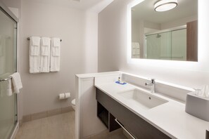 Une salle de bain moderne avec une douche à parois de verre, un lavabo blanc avec un miroir au-dessus et un porte-serviettes avec plusieurs serviettes.