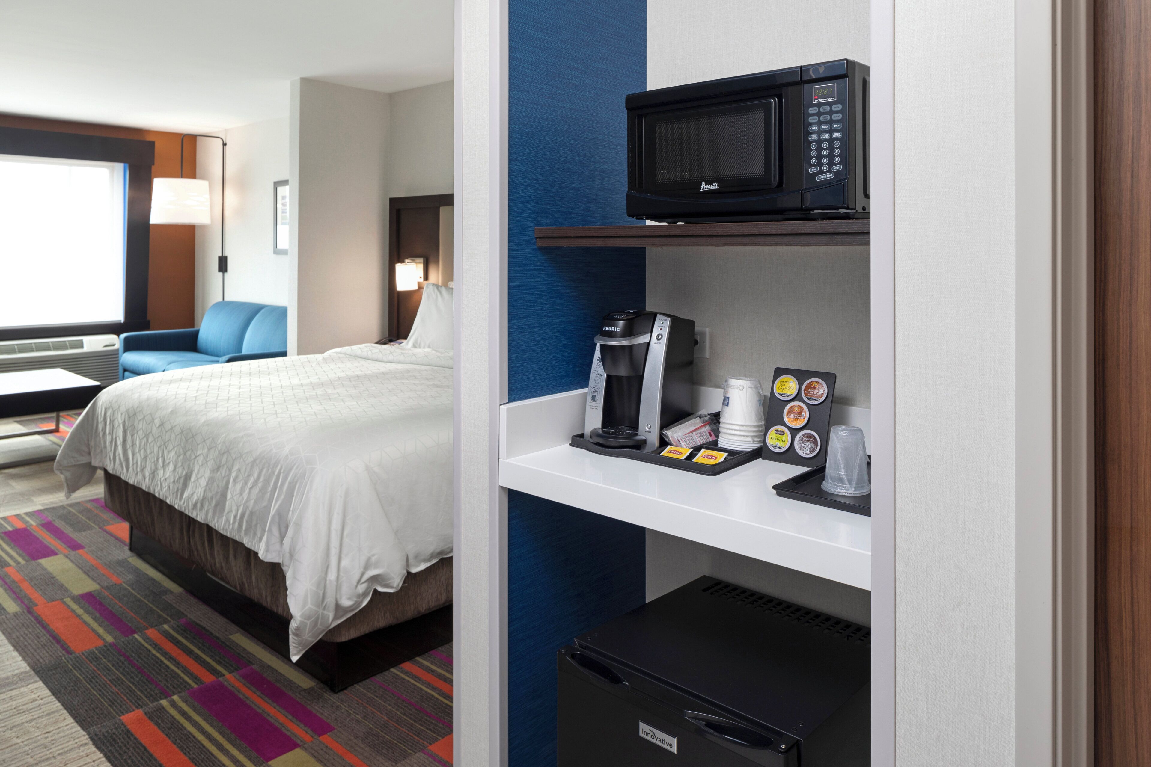 A hotel room with a bed, a coffee machine, a microwave, and a mini-fridge.