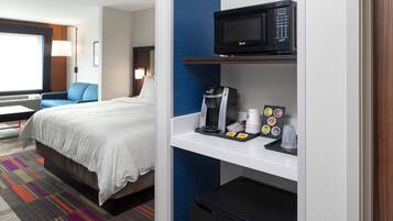 A hotel room with a bed, a coffee machine, a microwave, and a mini-fridge.
