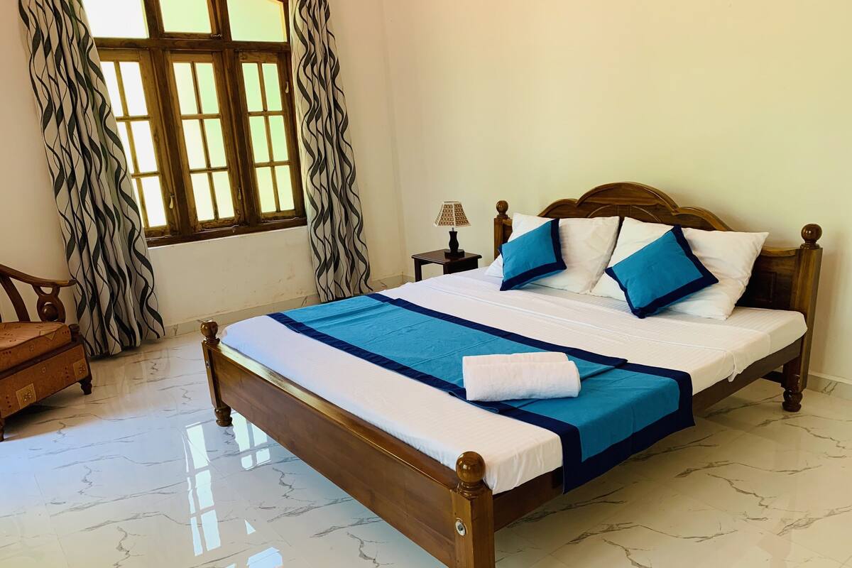A neatly made bed with a blue and white bedspread, a wooden headboard, and a nightstand with a lamp.