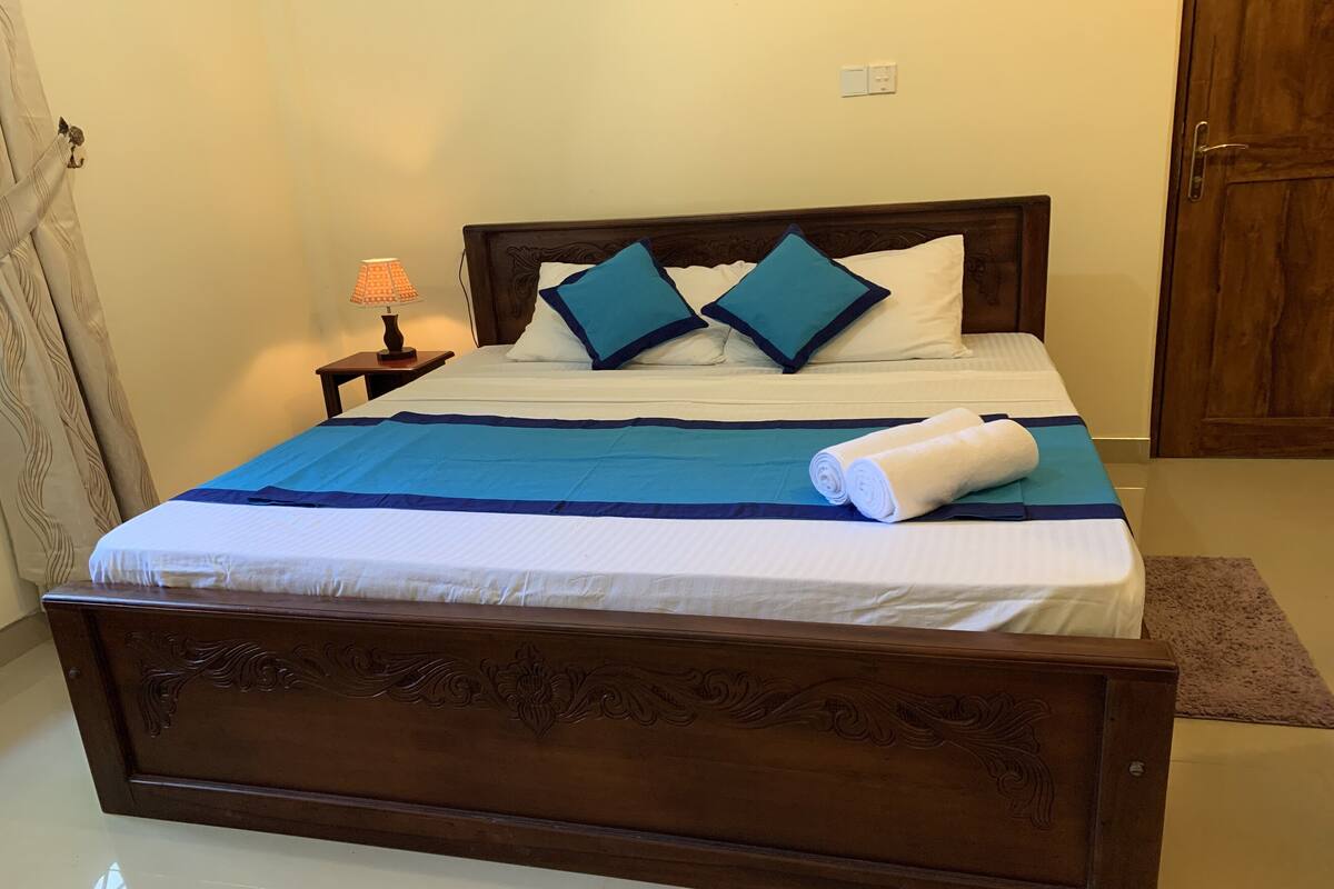 A neatly made bed with a blue and white bedspread, two blue pillows, and a rolled white towel.