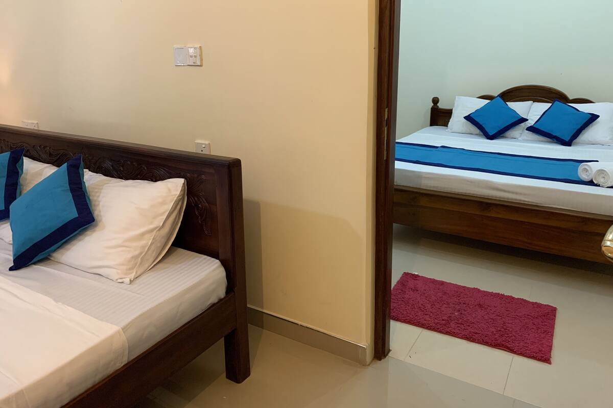A room with a bed, a wooden headboard, a red rug, and a white wall with a power outlet.