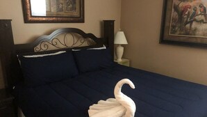 Un letto con una coperta blu scuro e un cuscino a forma di cigno bianco. Sopra il letto c'è un quadro incorniciato e un comodino con una lampada.