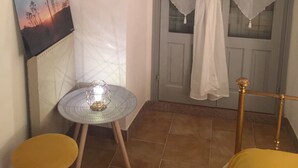 Una habitación pequeña con una mesa redonda, dos sillas amarillas, un cuadro en la pared y una puerta con cortinas blancas.