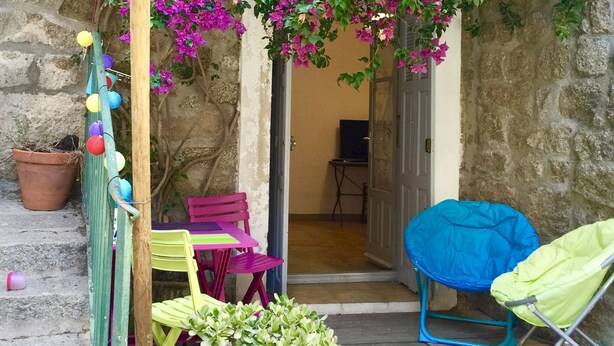 Un espacio al aire libre con paredes de piedra, una mesa y sillas de madera, una silla plegable azul y una planta en maceta.