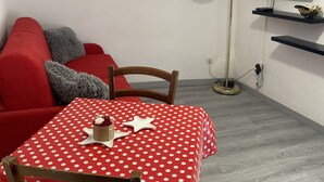 Un pequeño espacio de sala con un sofá rojo, una mesa de lunares y un televisor montado en la pared.