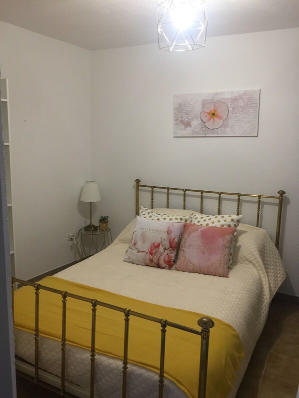 A neatly made bed with a yellow bedspread and two pillows, a bedside table with a lamp, and a wall-mounted flower painting. - Small nest in the heart of the old town (Sartène)
