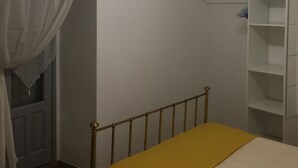Un dormitorio con cama, armario, lámpara en el techo y ventana con cortinas.
