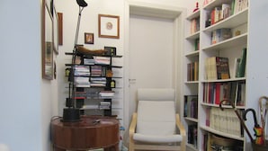 Une salle d’étude avec un bureau en bois, un fauteuil blanc et deux étagères remplies de livres et d’objets décoratifs.