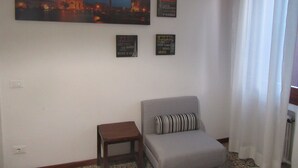 Un salon avec un canapé, une petite table et un tableau représentant un paysage urbain. Il y a quatre panneaux accrochés au mur, dont l’un mentionne Paris.