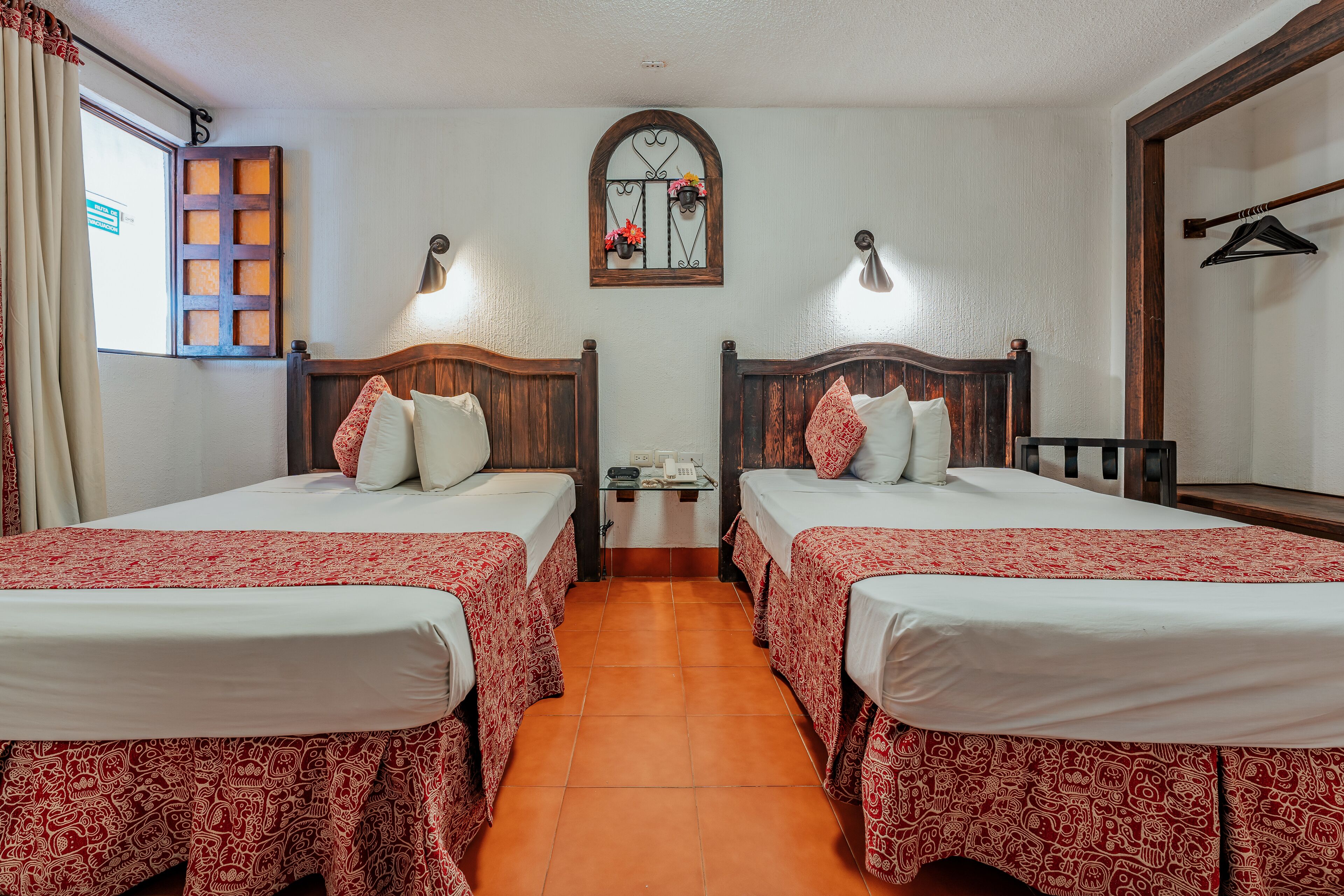 A hotel room with two beds, a wooden headboard, a small table, and a window with curtains.