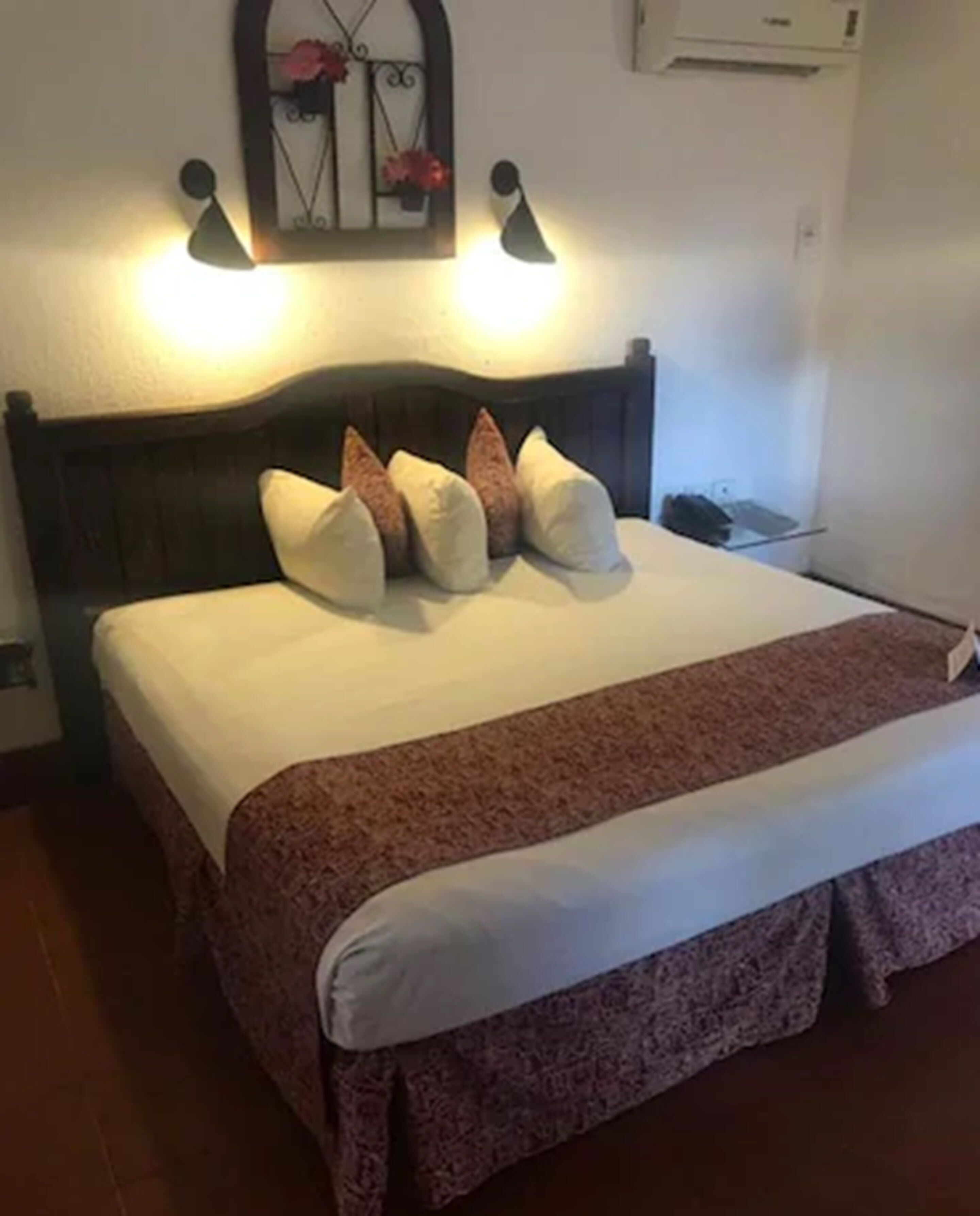 Un lit bien fait, recouvert d’une couvre-lit à motifs, avec une tête de lit en bois foncé et deux lampes fixées au mur.