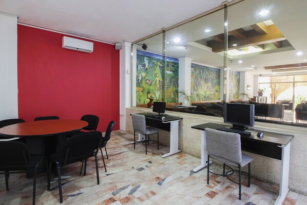 A conference room with a red wall, a large window with a mural, a round table with chairs, and a computer desk with a monitor and keyboard. - Hotel Maya Yucatán (Mérida)