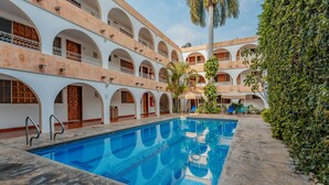 A swimming pool with a clear blue water surface, surrounded by a multi-story building with arched windows and balconies. - Hotel Maya Yucatán (Mérida)