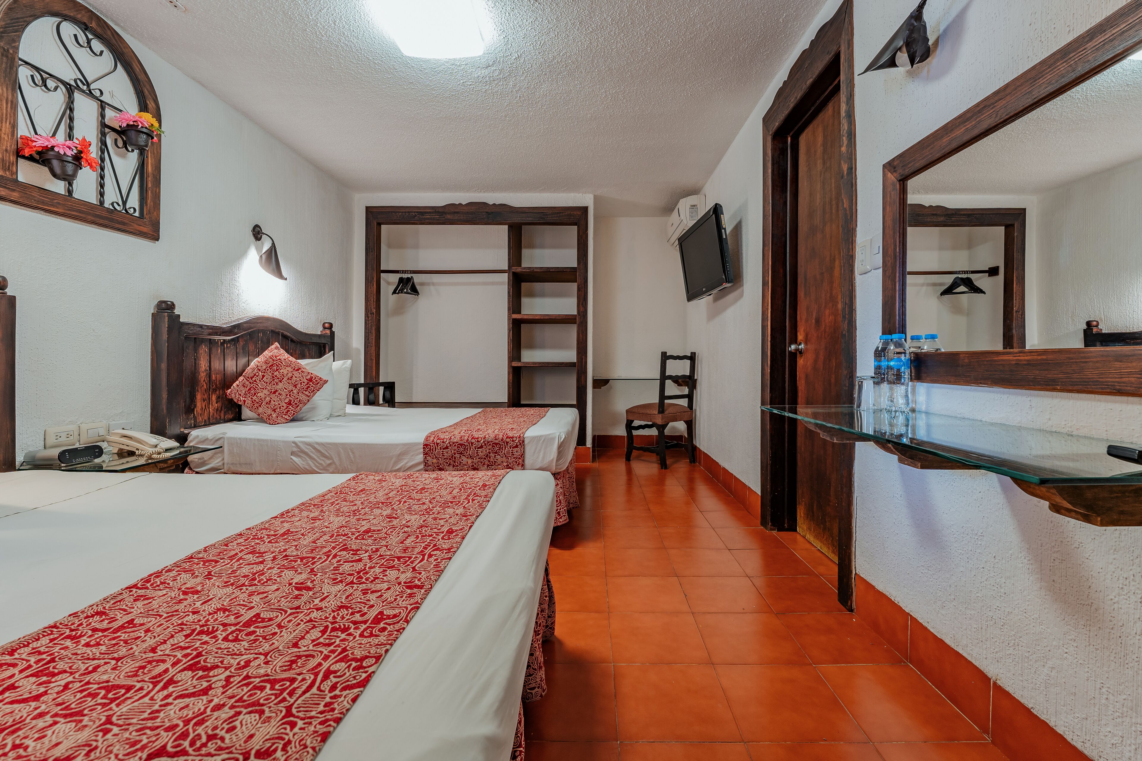 A hotel room with two beds, a TV, a mirror, and a glass shelf.