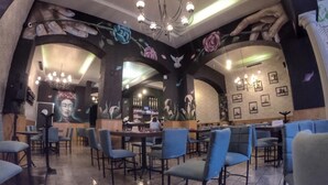 A restaurant interior with blue chairs, a bar area, and floral wall art. - Hotel Maya Yucatán (Mérida)