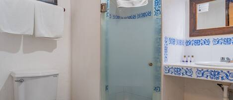 A bathroom with a toilet, a glass shower enclosure, and a sink with blue decorative tiles.