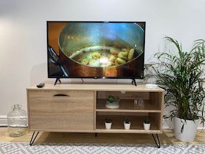 A television on a wooden TV stand with a remote, a small plant, and a glass jar.