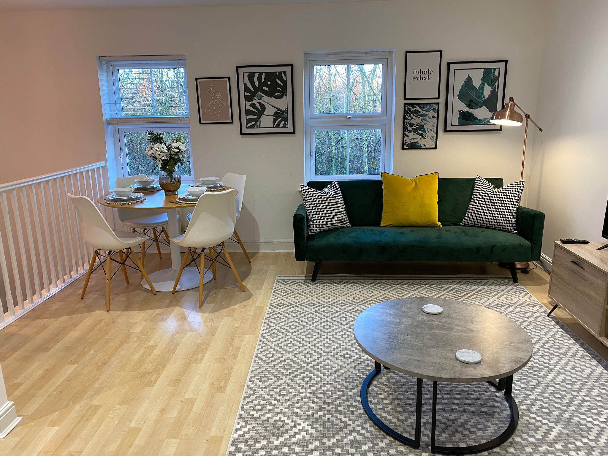 A modern living room with a green sofa, white chairs, a dining table, and artwork on the walls.