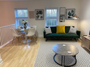 En moderne stue med en grøn sofa, hvide stole, et spisebord og kunst på væggene.