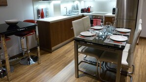 Une cuisine moderne avec un coin repas, comprenant des appareils en acier inoxydable, un tabouret de bar et une table à manger en verre pour deux personnes.