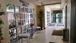 Zona de recepción de un hotel con separador de vidrio, mostrador de recepción, sillas y plantas en macetas.