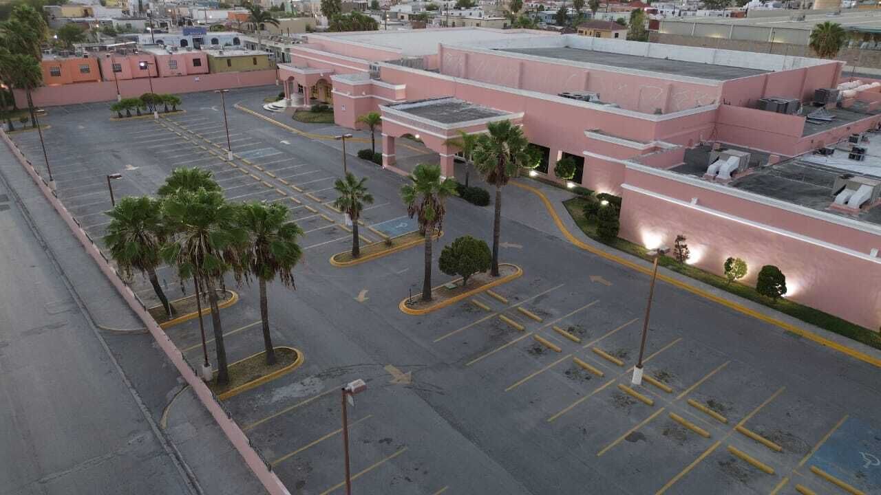 Un estacionamiento con espacios delimitados y palmeras, junto a un edificio de fachada rosa y varios pisos.