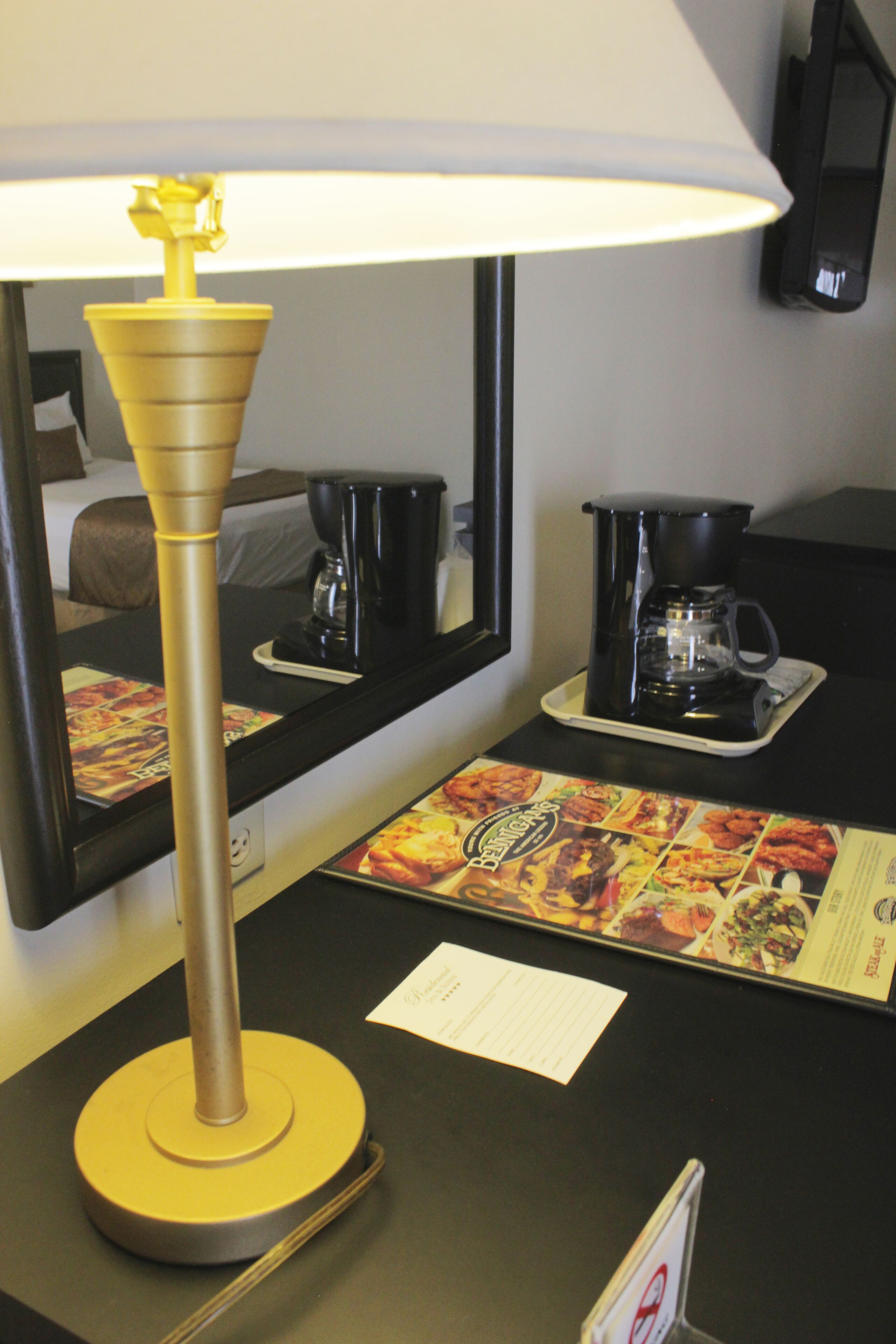 A hotel room with a lamp, a coffee maker, a menu, and a mirror.