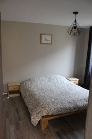 Une chambre à coucher avec un lit, des tables de chevet en bois, un luminaire suspendu et un tableau encadré au mur.