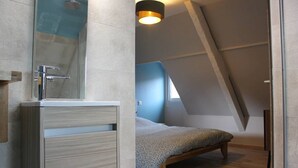A modern bedroom with a skylight, a wooden bed, and a bathroom with a modern sink and shower.